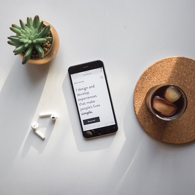Mobile phone on a desk beside a plant and a beverage